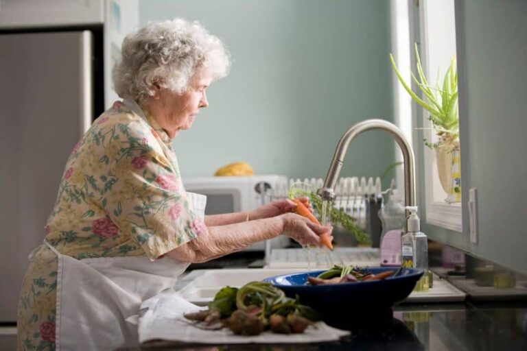 A senior washing vegetables in a kitchen sink