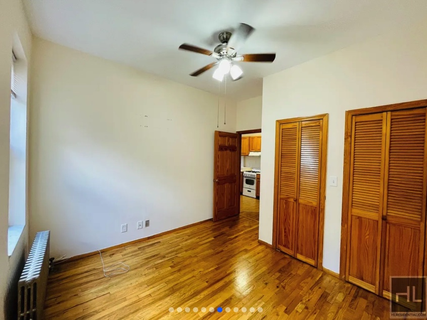 apartment listing photo of empty bedroom with two closet spaces and kitchen in the background