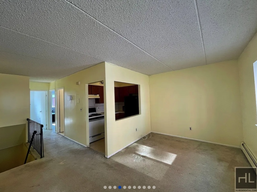 apartment listing photo of empty living room and kitchen with staircase