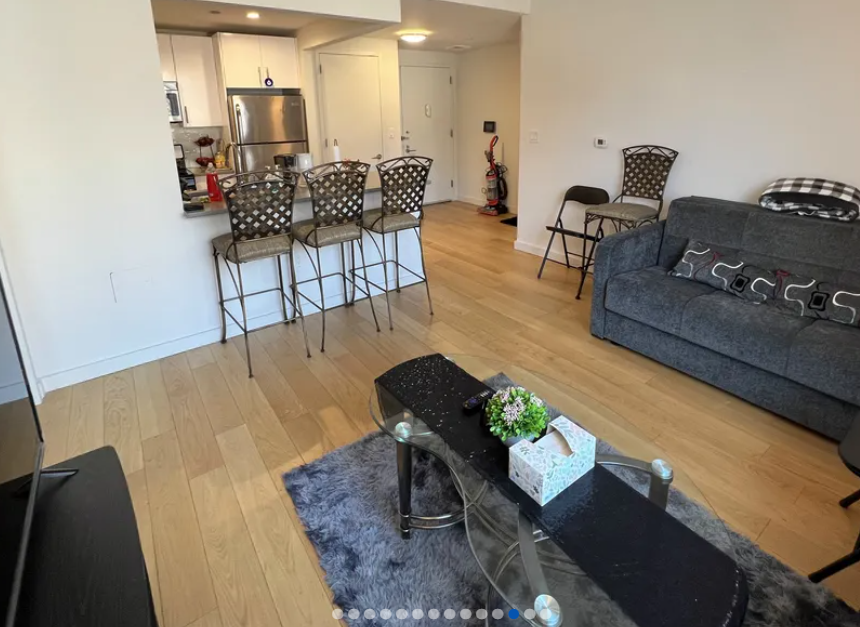 apartment photo of furnished living room with coffee table, couch, and kitchen in the background